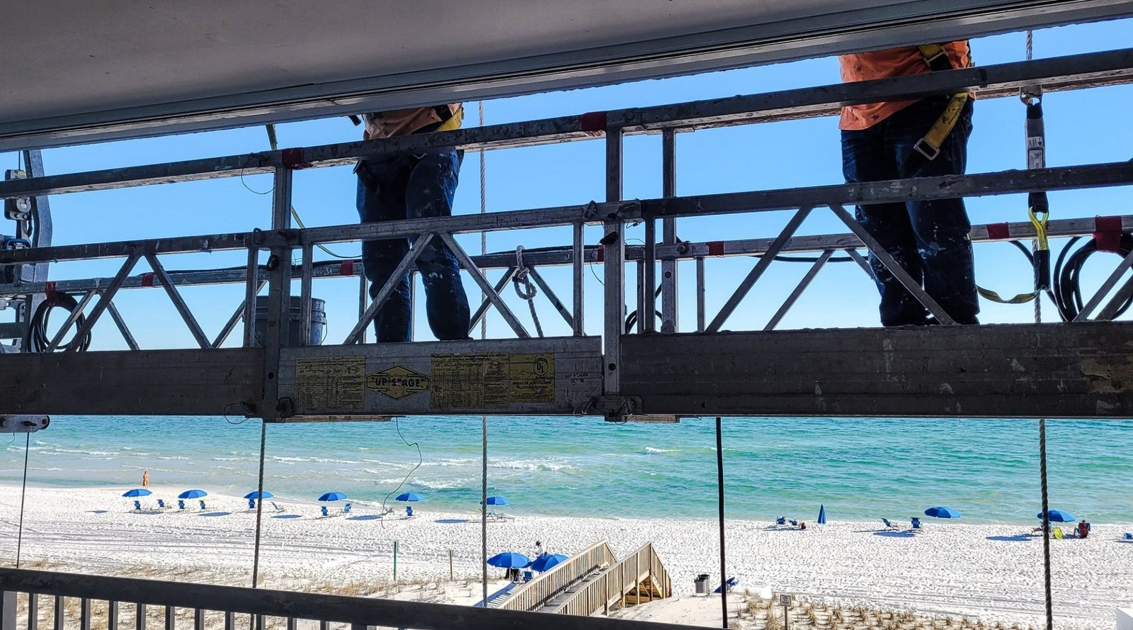 Two workers painting the outside of a condo building with their backs to the beach.