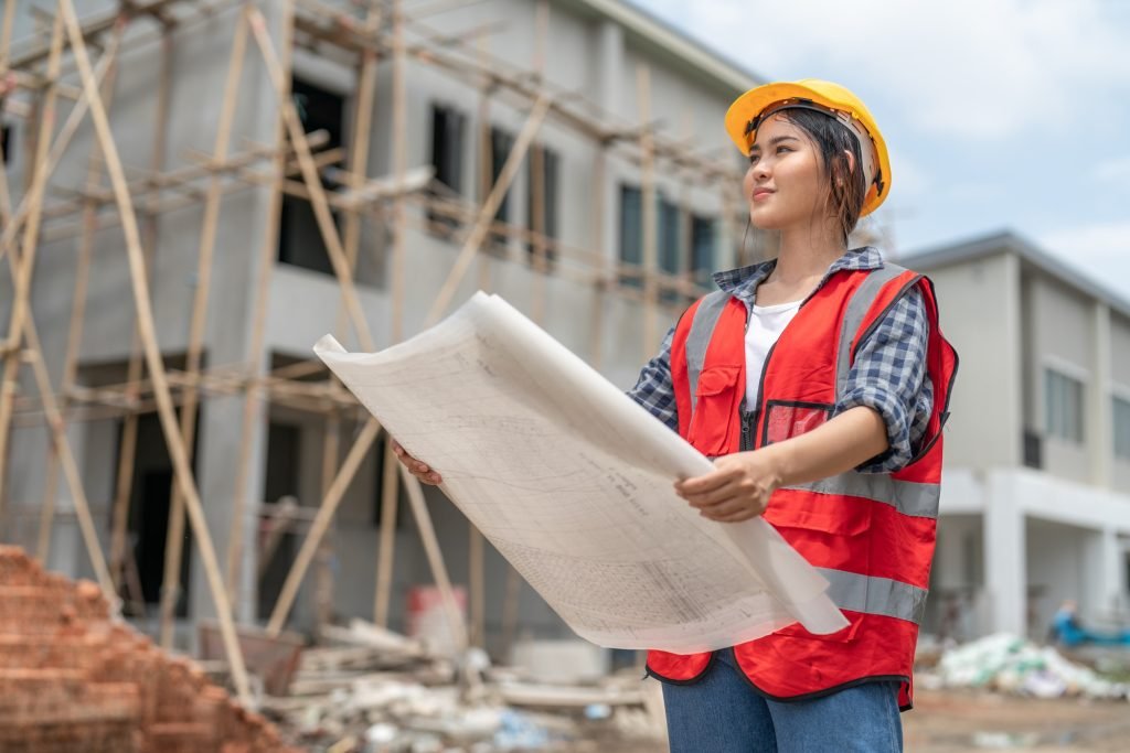 Asian female civil engineer holding blueprints housing estate project working at construction site