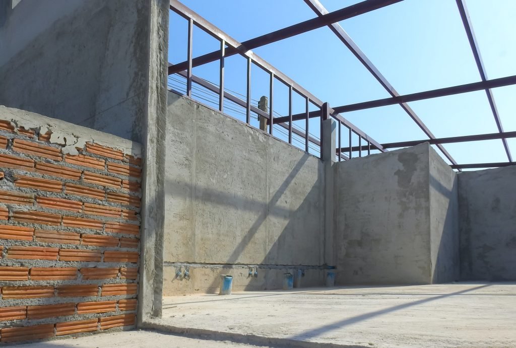 Concrete wall structure inside of room with metal shed roof framing under construction