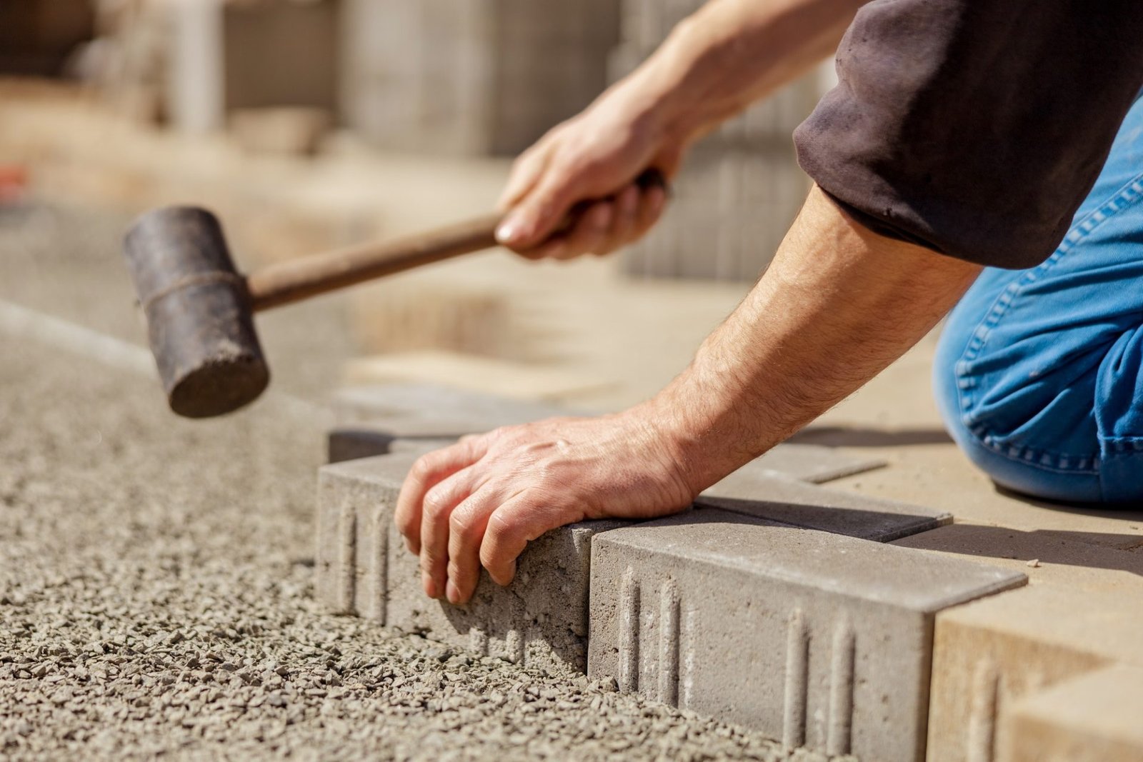 Young man laying grey concrete paving slabs in house courtyard on gravel foundation base.