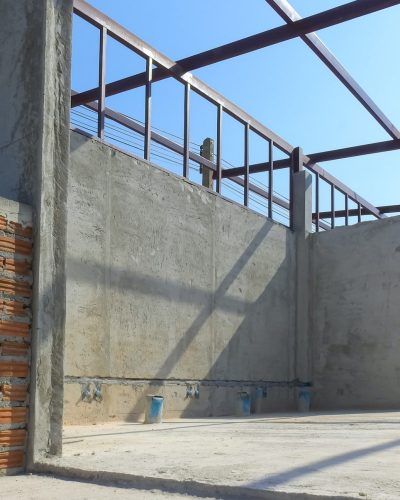 Concrete wall structure inside of room with metal shed roof framing under construction