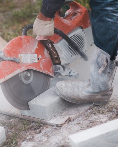 Worker mason cuts the sidewalk tile with circular saw while repairing sidewalk in city street